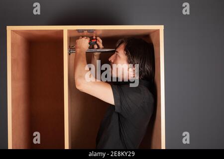 Ein Mann dreht ein Rohr für einen Aufhänger in einem Schrank mit einem Schraubendreher. Die Querlatte zum Aufhängen der Kleidung. Stockfoto