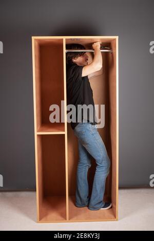 Ein Mann dreht ein Rohr für einen Aufhänger in einem Schrank mit einem Schraubendreher. Die Querlatte zum Aufhängen der Kleidung. Stockfoto