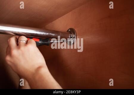 Ein Mann dreht ein Rohr für einen Aufhänger in einem Schrank mit einem Schraubendreher. Die Querlatte zum Aufhängen der Kleidung. Stockfoto