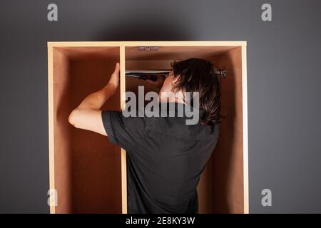 Ein Mann dreht ein Rohr für einen Aufhänger in einem Schrank mit einem Schraubendreher. Die Querlatte zum Aufhängen der Kleidung. Stockfoto