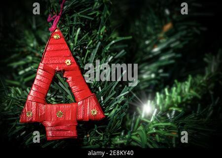 Extreme Nahaufnahme eines kleinen und roten Weihnachtsbaums aus gewebtem Stroh, der an einem grünen Weihnachtsbaum hängt. Stockfoto