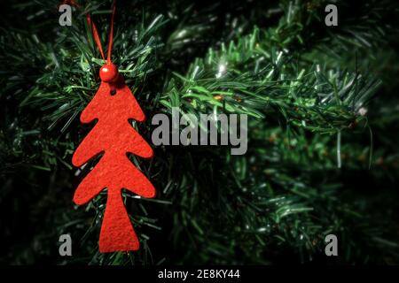 Extreme Nahaufnahme eines kleinen roten Weihnachtsbaums aus Samt, der an einem grünen Weihnachtsbaum hängt. Stockfoto
