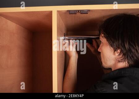 Ein Mann dreht ein Rohr für einen Aufhänger in einem Schrank mit einem Schraubendreher. Die Querlatte zum Aufhängen der Kleidung. Stockfoto
