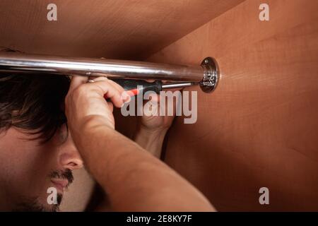 Ein Mann dreht ein Rohr für einen Aufhänger in einem Schrank mit einem Schraubendreher. Die Querlatte zum Aufhängen der Kleidung. Stockfoto