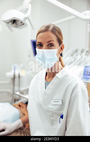 Porträt einer Zahnärztin beim Betrachen der Kamera. Zahnarzt trägt eine schützende Gesichtsmaske in ihrem Büro. Stockfoto