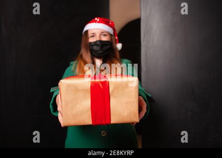 Lieferung nach Hause, Weihnachtsgeschenk für Neujahr. Weihnachten mit Coronavirus, eine Frau in einer Schutzmaske vor einer Pandemie. Geschenkversand, Online-Shopping Stockfoto