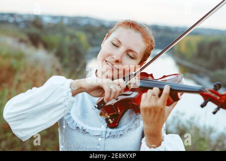 Schönes Mädchen spielen Geige in weißen Kleid im Wald Stockfoto