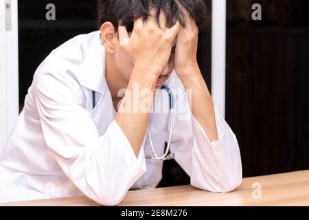 Ein Arzt legte seine Hand auf seinen Kopf, als er gestresst war. Überarbeiteter Arzt im Krankenhaus. Weil er zu hart arbeitet. Stockfoto