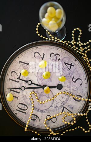 Eine Uhr, die nur wenige Minuten vor dem neuen anzeigt Die Jahre kommen neben zwölf Trauben Stockfoto