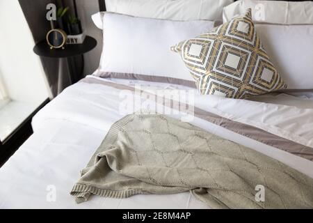 Komfortables Bett mit weichen Kissen, Laken, Decke stricken. Mit matal loft Tisch, Uhr eingerichtet, kleinen Pflanzen und schönen Design der Leuchte. Sz Stockfoto