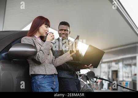 Glückliches multiethnisches Paar oder Geschäftskollegen, afrikanischer Mann und kaukasische Frau halten Pappbecher mit Kaffee und mit Tablet und Laptop-pc, während Stockfoto