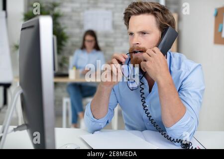 Männlicher Büroangestellter kaut seine Brille, während er sich konzentriert Stockfoto