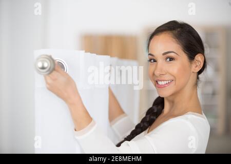 Frau, die seine weißen Vorhänge am Fenster aufhängte Stockfoto