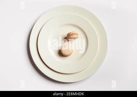 Zwei helle Makronen in einer hellen Platte auf einem hellen Hintergrund, minimalistische Komposition, Draufsicht Stockfoto