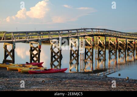 Kajaks an der Küste unter einer hölzernen Promenade in der frühen Abendsonne im Sommer Stockfoto