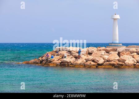 Ayia Napa, Zypern - 12. Juni 2018: Fischer sind auf Wellenbrecher in der Nähe des weißen Leuchtturms, Agia Napa Marina Stockfoto