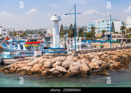 Ayia Napa, Zypern - 12. Juni 2018: Agia Napa Marina Blick mit festgetäuten Booten und weißem Leuchtturm Turm auf einem Wellenbrecher, Touristen zu Fuß in der Nähe Stockfoto