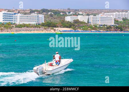 Ayia Napa, Zypern - 12. Juni 2018: Weißes Vergnügungsmotorboot mit Fahrer fährt an der Agia Napa Bucht bei sonnigem Tag, Rückansicht Stockfoto