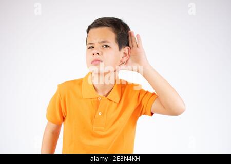 Was? Ich kann dich nicht hören. Portrait des aufmerksamen neugierigen kleinen Jungen, der Hand in der Nähe des Ohres hält und aufmerksam zuhört, was Sie sagen Stockfoto