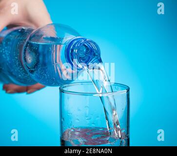 Wasser in ein Glas auf hellblauem Hintergrund gießen. Nahaufnahme, Seitenansicht. Stockfoto