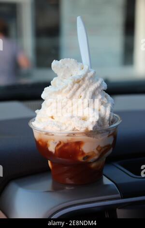 Große heiße Karamell sundae gekrönt mit flauschigen Schlagsahne sitzen Auf dem Armaturenbrett eines Autos Stockfoto