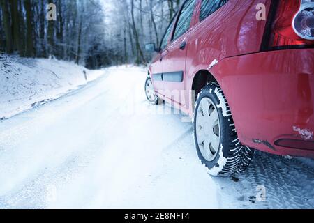 Rotes Auto fahren auf Schnee im Winter auf einer kurvigen Landstraße im Wald, Konzept für den Sicherheitsverkehr bei schlechtem Wetter und Gefahr von rutschigen Bedingungen, CO Stockfoto