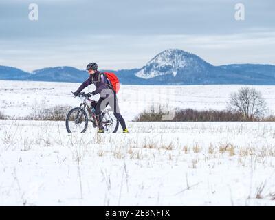 Mountainbiker in verschneite Landschaft. Sportler richtig für den Winter Radfahren ausgestattet ist im schweren Gelände zu befreien. Sonniges Winterwetter und Schnee. Stockfoto