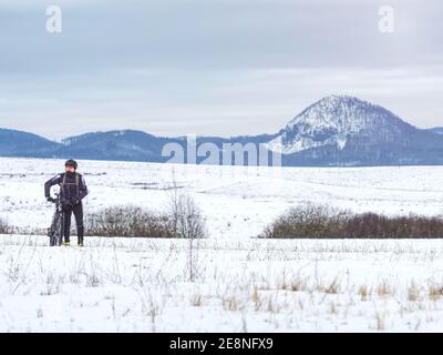 Mann Biker schob Mountainbike in Schneewehe. Frost sonniges Winterwetter. Biker schiebt Fahrrad allein im Tiefschnee Stockfoto