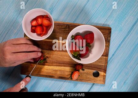 Blick von oben auf einen Mann, der plump Erdbeeren auf einem hölzernen Schneidebrett schneidet. Stockfoto