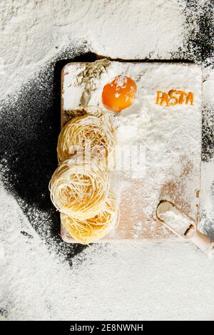 Frisch gekochte Pasta liegt auf einer dunklen, mit Mehl bestäubten Oberfläche. Italienische Pasta. Tagliatelle. Rohe Pasta. Italienische Pasta Rezept. Draufsicht, Kopierbereich. Stockfoto