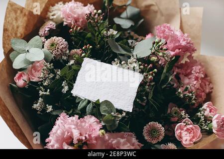 Moody feminine Hochzeit, Geburtstag Mockup Szene. Nahaufnahme von leerem Baumwollpapier Karte, Einladung auf rosa Blumenstrauß. Eustoma, santini Mütter und Stockfoto