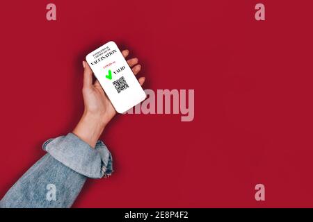 Frau Hand hält Smartphone mit gültigen digitalen Impfpass - Digitaler Impfpass für COVID-19 auf rotem Hintergrund mit Stockfoto
