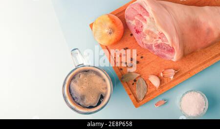 Rohe Schweinshaxe, Knoblauch, Zwiebel, getrocknete Lorbeerblätter, Meersalz und Pfefferkörner auf Holzschneidebrett. Draufsicht. Speicherplatz kopieren. Stockfoto