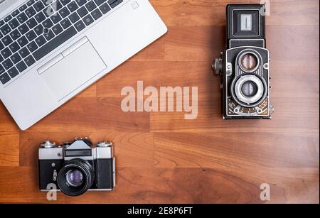 Eine alte Spiegelreflexkamera aus dem Jahr 35mm und eine alte Mittelformat-Spiegelreflexkamera, von oben gesehen, mit einem modernen Laptop daneben, horizontal Stockfoto