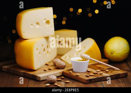Käse auf dem Tisch, dunkler Hintergrund. Mittelharter Käsekopf edam, gouda, Parmesan mit Honigglas auf Holzschneidebrettern. Gesunde Ernährung Konzept Stockfoto