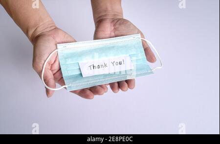 Dankesnotiz auf der Oberseite der Gesichtsmaske, auf der Handfläche des Mannes. Anerkennung für Frontliner und medizinisches Personal für den Kampf gegen Covid-19. Stockfoto