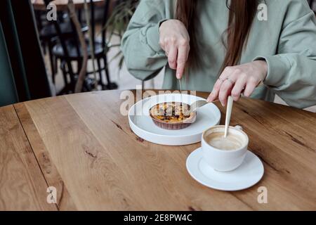 Mädchen beim Frühstück in einem Café. Eine unkenntliche Frau schneidet ihre Pilzquiche, um sie mit einem Kaffee zu essen. Menschen und Essen Konzept. Stockfoto