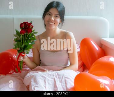 Valentinstag. Glückliches Mädchen am Morgen auf dem Bett hält einen Strauß Rosen. Stockfoto