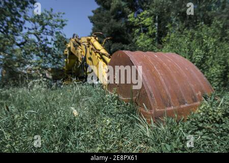 Alte verlassene Bagger mit großen rostigen Schaufel im Vordergrund Umgeben von grünen Pflanzen Stockfoto