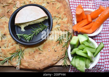 Focaccia ist ein italienisches Hefebrot, das in einer flachen Pfanne gebacken wird Der Teig wird mit Olivenöl mit Rosmarin gekrönt gewürzt Serviert mit Gurken Karotten Sellerie Stockfoto