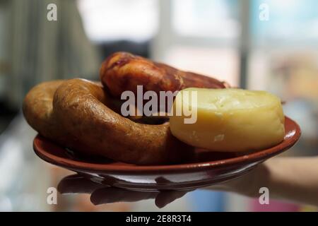 Hand hält einen Teller mit Weichkäse und portugiesischen Würsten Stockfoto