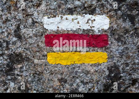 Wegmarkierungsschild mit weißen, roten und gelben Streifen an der Wand bemalt Stockfoto