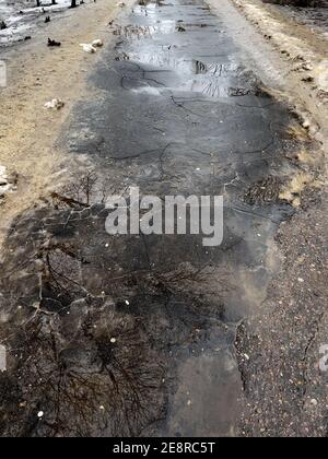 Nahaufnahme des Gehwegs mit Pfützen in der Frühjahrssaison. Zerstörte Straße mit geschmolzenem Schnee und schmutzigem Schnee an den Rändern Stockfoto