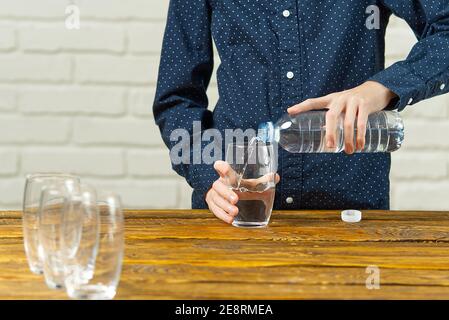 Junge gießt Wasser aus der Plastikflasche in die Glas auf Holztisch Stockfoto