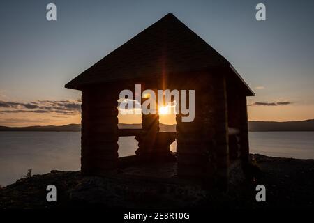 Haus Pavillon auf dem felsigen Ufer eines malerischen Sees In den Strahlen des Sonnenuntergangs Stockfoto