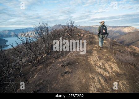 Ein Wanderer mit Blick weg und zu Fuß in die Ferne entlang der Kamm eines Hügels mit Blick auf einen See und Berge, in Kalifornien. Stockfoto