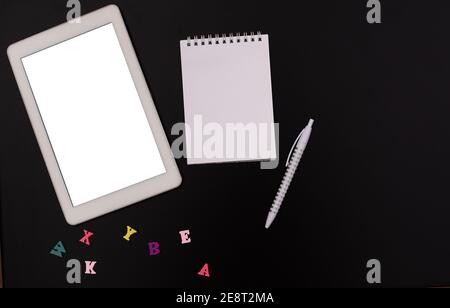 Online-Kurse. Das Studium der englischen Sprache. Ein Tablett mit einer Kopie des Platzes, einem leeren Notizblock, einem Stift, Buchstaben auf schwarzem Hintergrund. Stockfoto