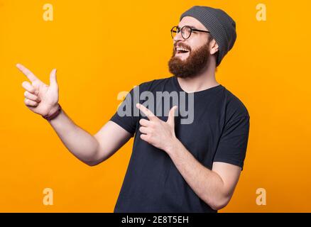 Ein glücklicher junger Mann mit Bart lächelt und zeigt mit den Fingern auf einen freien Raum. Stockfoto