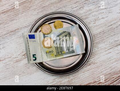 Overhead-Aufnahme von fünf Euro-Banknoten und schmutzigen Euro-Münzen Auf einer silbernen Platte Stockfoto