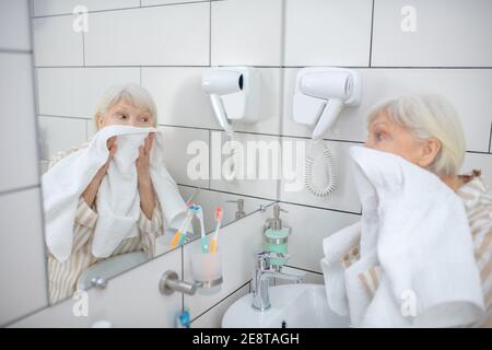 Grauhaarige Frau, die ihr Gesicht mit dem Handtuch trocknet Stockfoto